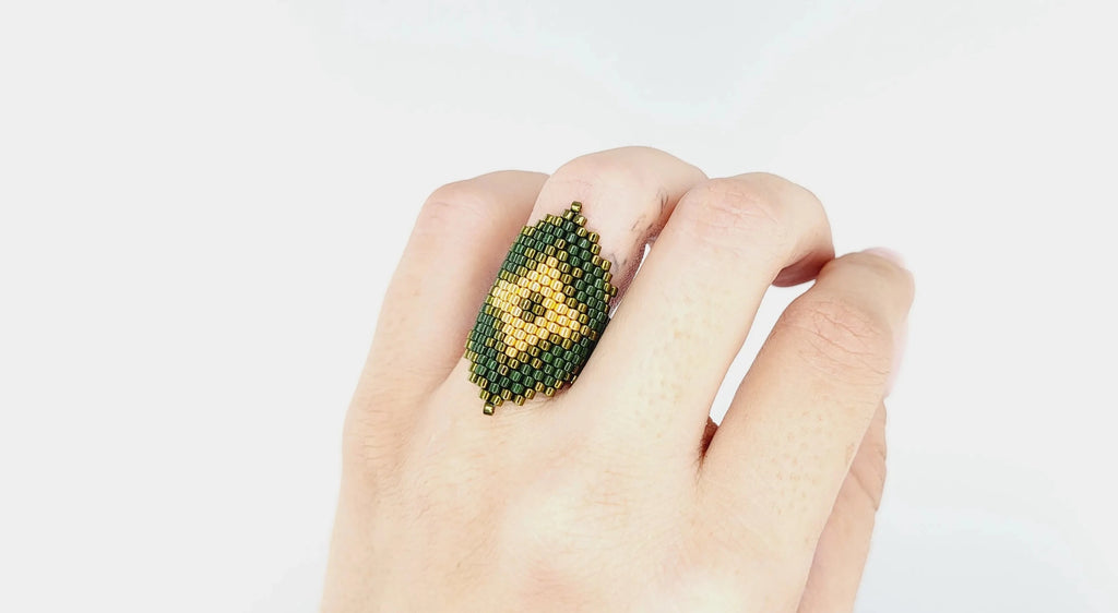 Modelo con un anillo cosido con cristal japonés verde brillante, mate y dorado
